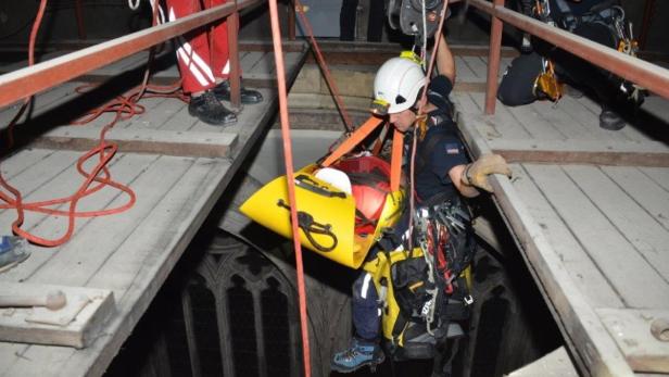 Ein Rettungssanitäter seilt eine Person in einer gelben Trage von einem hohen Gebäude ab.