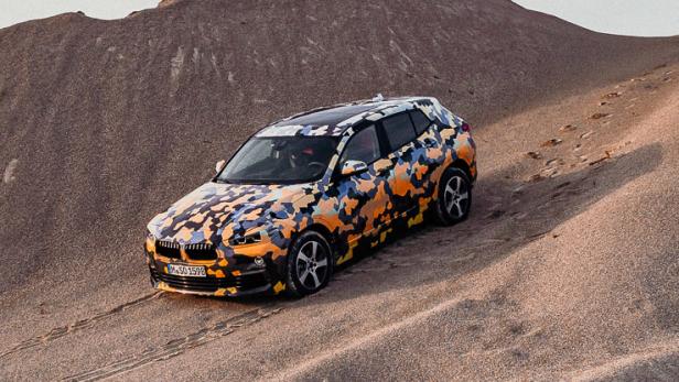 Ein BMW mit Tarnmuster fährt eine Sanddüne hinauf.