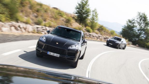 Zwei schwarze Porsche Cayenne fahren auf einer kurvenreichen Bergstraße.