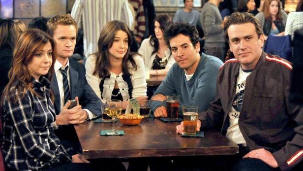 Die Freunde aus der Serie „How I Met Your Mother“ sitzen in einer Bar an einem Tisch.