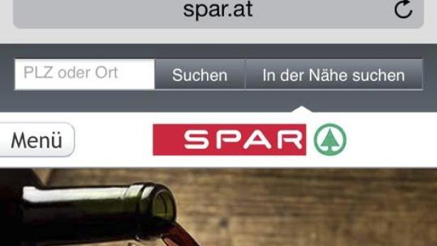Die Webseite von Spar Österreich auf einem Smartphone mit Weinflasche im Hintergrund.