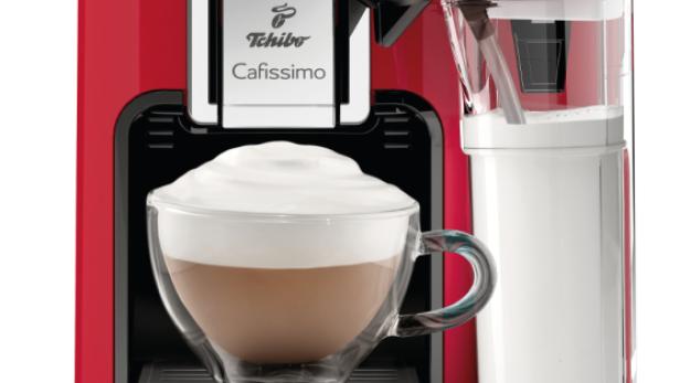 Eine rote Saeco Tchibo Cafissimo Kaffeemaschine mit einer Tasse Cappuccino und einem Milchbehälter.