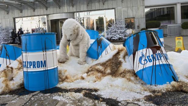 Ein Eisbär zwischen blauen Fässern mit der Aufschrift „Gazprom“ und Ölverschmutzung.