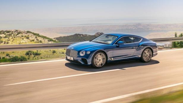 Ein blauer Bentley Continental fährt auf einer Küstenstraße.