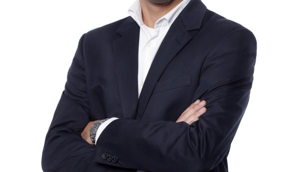 Ein Mann im Anzug lächelt mit verschränkten Armen.