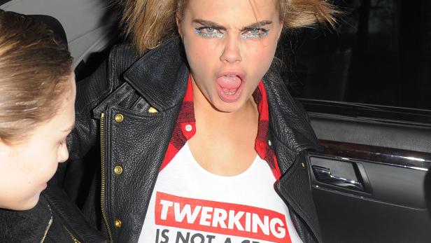 Cara Delevingne sitzt in einem Auto und zeigt ein T-Shirt mit der Aufschrift „Twerking is not a crime“.
