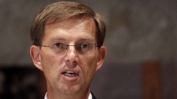 Ein Mann mit Brille spricht vor einem dunklen Hintergrund.