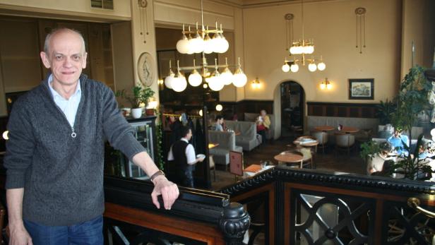 Ein Mann steht in einem eleganten Café mit Gästen und Kronleuchtern.