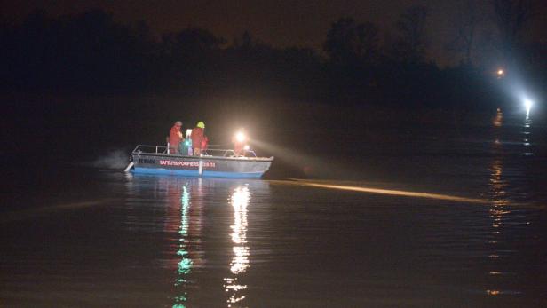 Ein Boot der Feuerwehr mit Suchscheinwerfer ist nachts auf dem Wasser unterwegs.