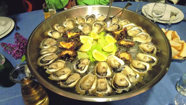 Eine Platte mit frischen Austern, Zitronenspalten und Brot auf einem Tisch.