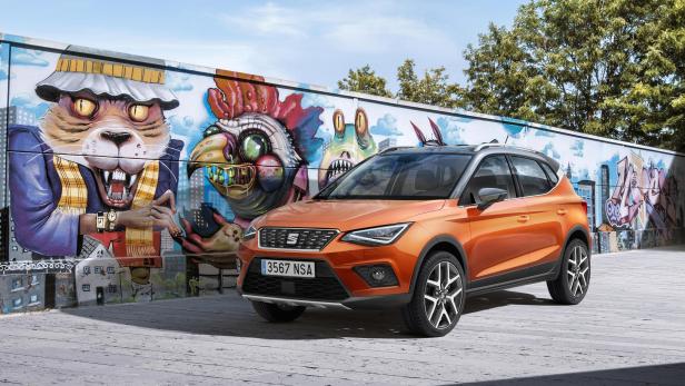 Ein orangefarbener Seat Arona vor einer Wand mit Graffiti-Kunstwerken.