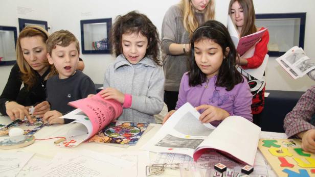 Eine Gruppe Kinder und Erwachsene sitzen an einem Tisch und beschäftigen sich mit Büchern und Spielen.