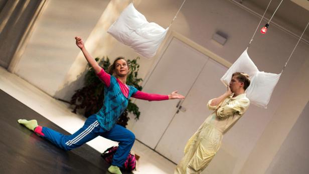Zwei Darsteller interagieren mit an Fäden hängenden Kissen auf einer Bühne.