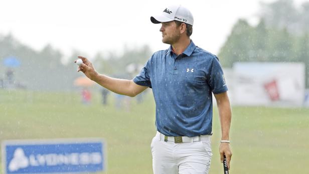 Ein Golfspieler hält bei Regen einen Golfball in der Hand.