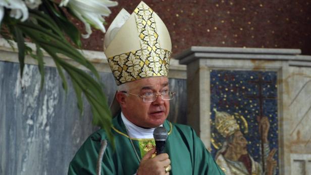 Ein Bischof mit Mitra hält ein Mikrofon in einer Kirche.