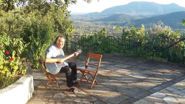 Gert Steinbäcker musiziert mit Gitarre vor seinem Haus auf Korfu.