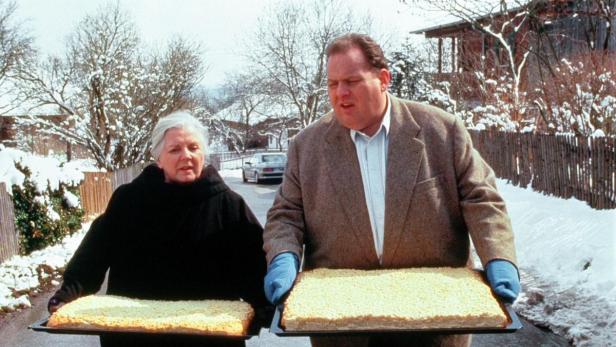 Ein Mann und eine Frau tragen im Winter jeweils ein Backblech mit Kuchen.