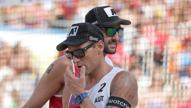 Zwei Beachvolleyballspieler mit Sonnenbrillen und Kappen auf dem Spielfeld.