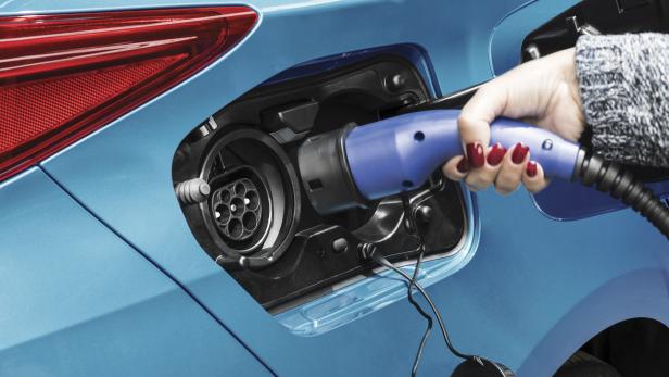 Eine Hand schließt ein blaues Ladekabel an ein blaues Elektroauto an.