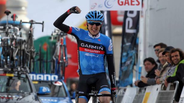 Ein Radrennfahrer im blauen Trikot jubelt mit erhobener Faust vor einer Zuschauermenge.