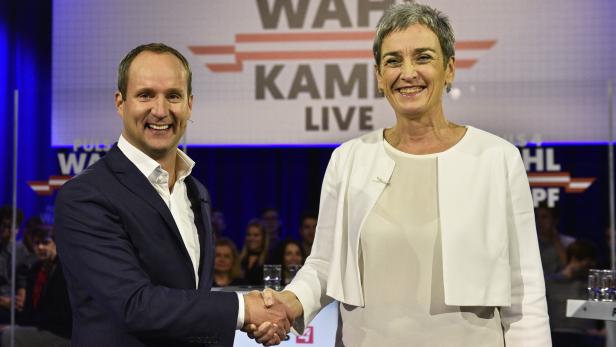 Zwei Personen schütteln sich vor einer Wahlkampfveranstaltung die Hände.