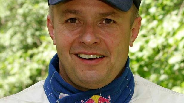 Ein Mann mit Basecap und blauem Tuch mit Red Bull Logo lächelt in die Kamera.