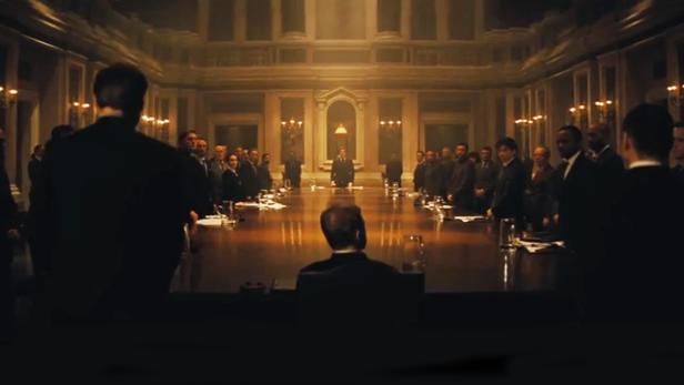 Eine lange Konferenztisch mit vielen Menschen in einem formellen Raum.