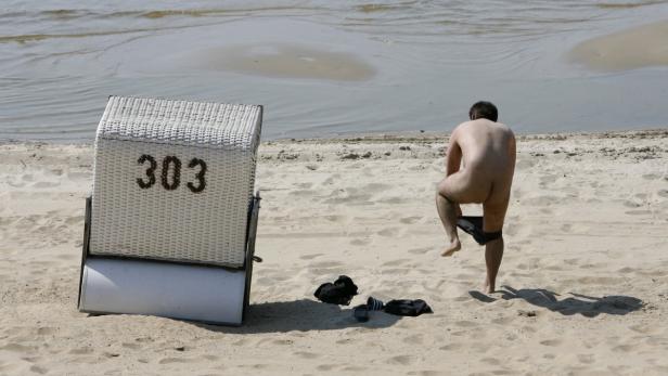 Ein Mann zieht sich am Strand neben einem Strandkorb mit der Nummer 303 um.