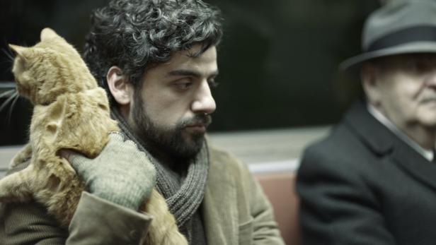 Oscar Isaac hält eine orangefarbene Katze im Arm, während er in der U-Bahn sitzt.
