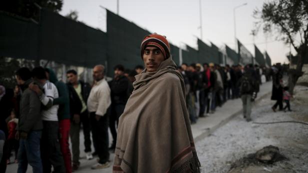 Ein Mann mit Mütze und Umhang steht vor einer Schlange von Menschen.