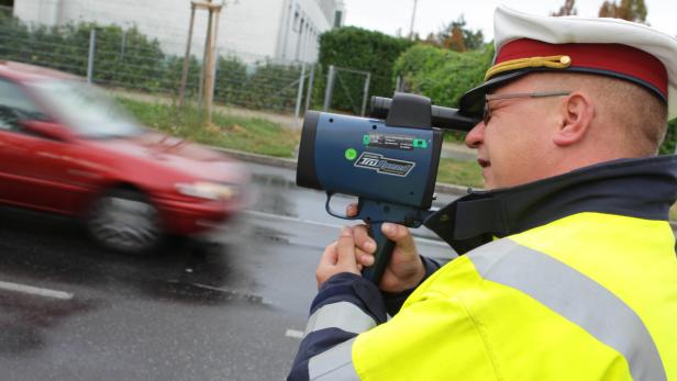 Ein Polizist misst mit einem Lasergerät die Geschwindigkeit eines vorbeifahrenden Autos.