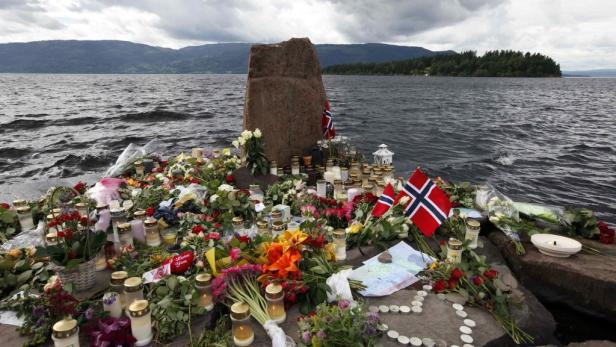 Blumen, Kerzen und norwegische Flaggen an einem Gedenkort am Wasser.