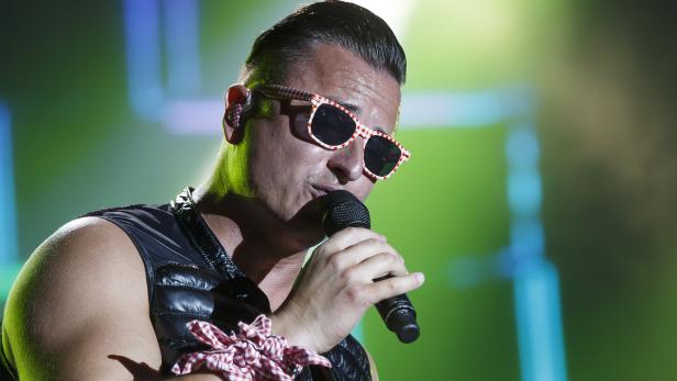 Ein Mann mit Sonnenbrille singt in ein Mikrofon.