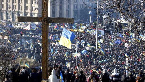 Eine große Menschenmenge mit ukrainischen Flaggen demonstriert auf einem Platz vor einem Holzkreuz.