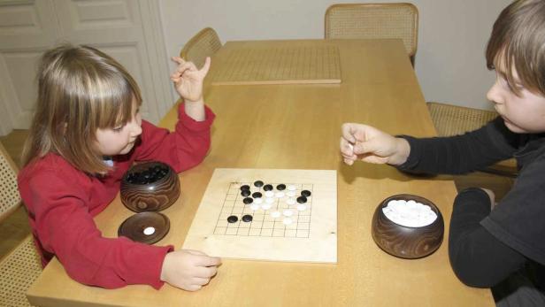 Zwei Kinder spielen das Brettspiel Go am Tisch.