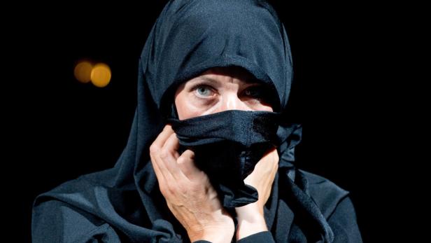 Eine Frau mit blaugrünen Augen verhüllt ihr Gesicht mit einem schwarzen Tuch.