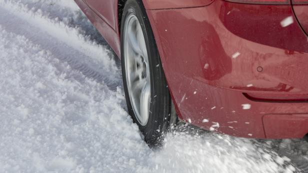 Ein rotes Auto fährt auf einer schneebedeckten Straße.