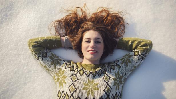 Beautiful caucasian woman lying in the snow, making a snow print and enjoying