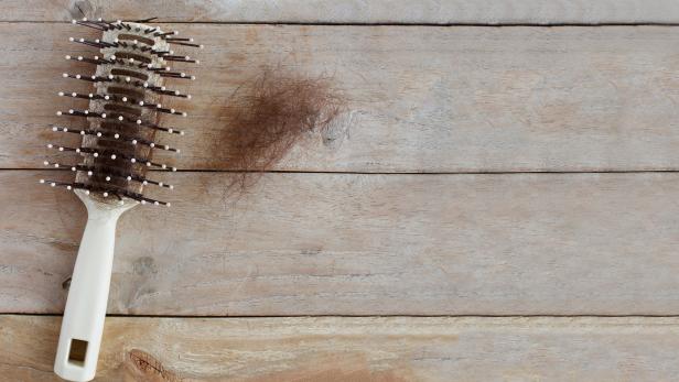 Eine Haarbürste mit Haaren liegt auf einem Holztisch.