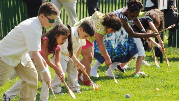 Eine Gruppe Kinder nimmt an einem Eierlauf mit Löffeln auf einer Wiese teil.