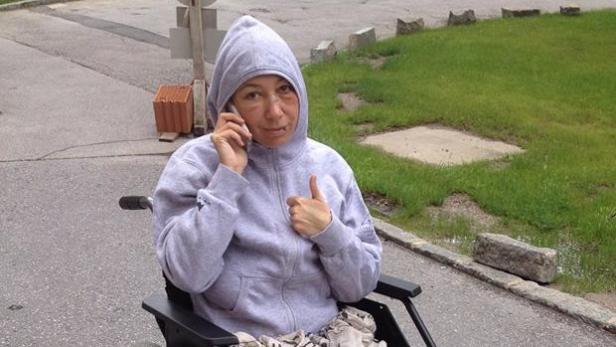 Eine Frau im Rollstuhl telefoniert und zeigt den Daumen nach oben.