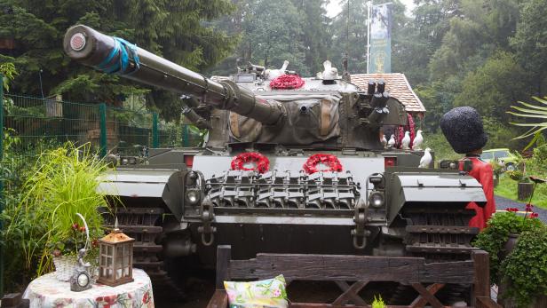Ein Panzer geschmückt mit Mohnblumen und Friedenstauben, rundherum Figuren
