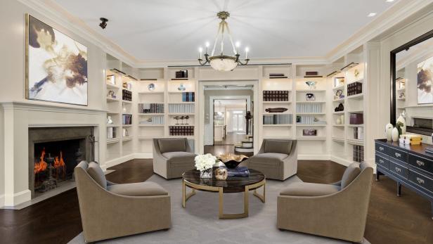 Ein Wohnzimmer mit Bücherregalen, einem Kamin und vier Sesseln um einen runden Tisch.