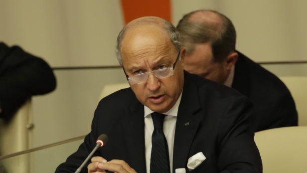 Ein Mann mit Brille und Anzug sitzt an einem Tisch mit Mikrofon.