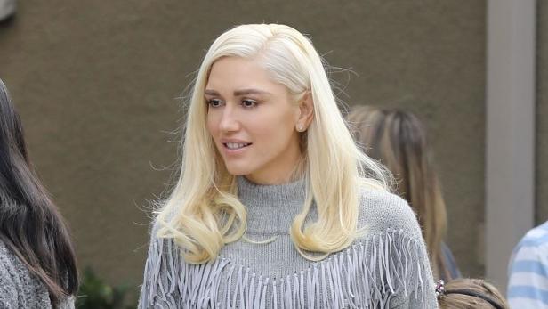 Gwen Stefani mit blonden, gewellten Haaren und einem grauen Fransenpullover.