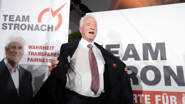 Frank Stronach öffnet seinen Anzug vor einem „Team Stronach“-Plakat.