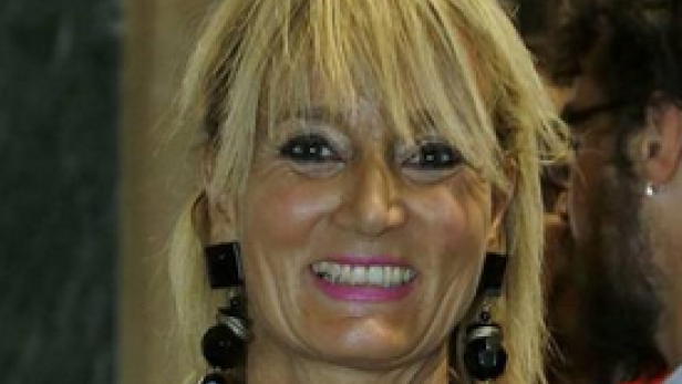 Eine Frau mit blonden Haaren und auffälligen Ohrringen lächelt in die Kamera.