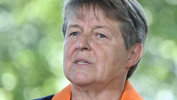 Nahaufnahme einer Frau mit kurzen grauen Haaren und einem orangefarbenen Oberteil.