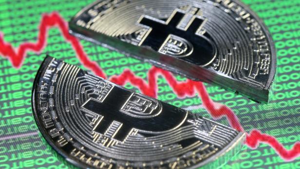 Zwei Bitcoin-Münzen liegen vor einem Diagramm mit fallenden Kursen.