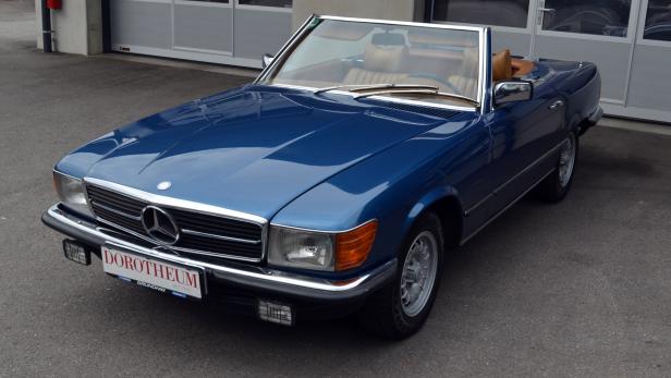 Ein blauer Mercedes-Benz SL Roadster der Baureihe R107 steht auf einem Parkplatz.